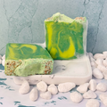 Green and yellow marbled soap bars on a stone surface with small stones around, Topped with pink Himalayan sea salt. 